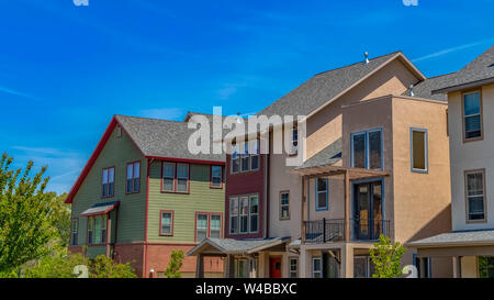 Panorama frame Exterior view of houses with vast blue sky background on a sunny day. Trees with lush green foliage can be seen in front of the homes. Stock Photo