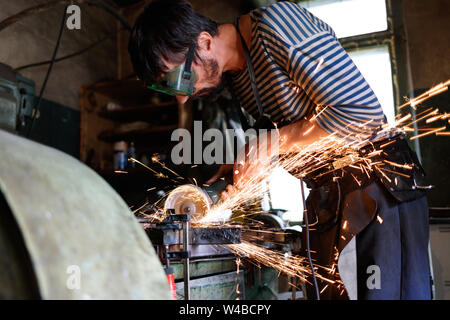 Professional blacksmith sawing metal with hand circular saw at forge. Stock Photo