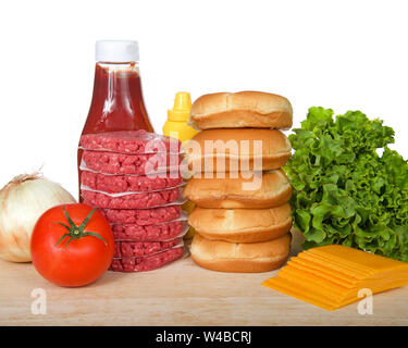 Raw hamburger patties stacked on wood table with buns, lettuce, cheese, tomato, onion, ketchup, mustard. Ingredients for a bbq lunch or dinner isolate Stock Photo