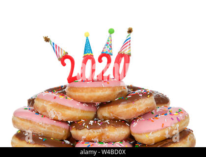 Variety of glazed donuts stacked with Happy 2020 candles wearing party hats, isolated on white. Happy New Year theme. Stock Photo