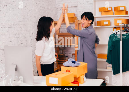 Side view of cheerful Asian entrepreneurs doing high five while working in office of online fashion business company Stock Photo