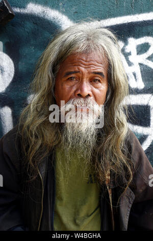 ANTIPOLO CITY, PHILIPPINES - JULY 19, 2019: A senior Filipino man with gray head and facial hair stand against a colorful wall and pose for the camera Stock Photo