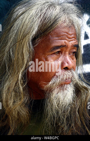 ANTIPOLO CITY, PHILIPPINES - JULY 19, 2019: A senior Filipino man with gray head and facial hair stand against a colorful wall and pose for the camera Stock Photo