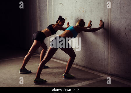 Two female athletes stretching against a concrete wall Stock Photo