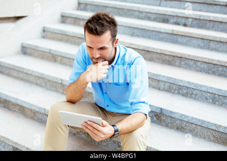 Photo of a student using a tablet and revising for his exam while sitting outdoors Stock Photo