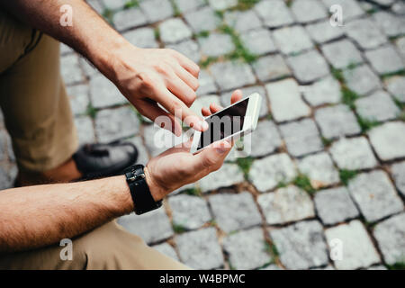 Close-up of a man sitting in the street and texting on his mobile Stock Photo
