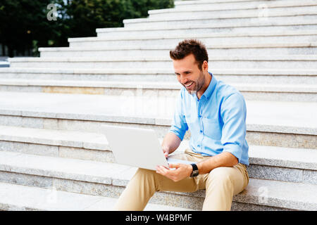 Handsome student sitting on stone stairs and using a laptop Stock Photo