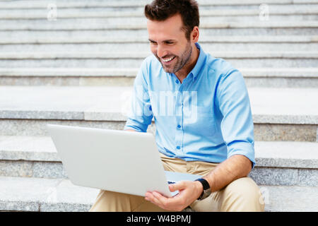 Happy student browsing the internet on his laptop and sitting outdoor Stock Photo