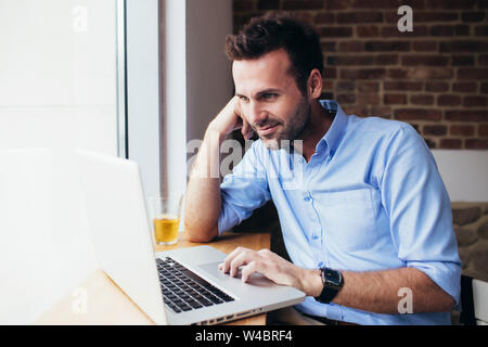 Cheerful young businessman sitting in cafe with laptop and working Stock Photo
