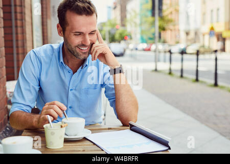 Happy man having coffee break at outdoors cafe, reading documents Stock Photo