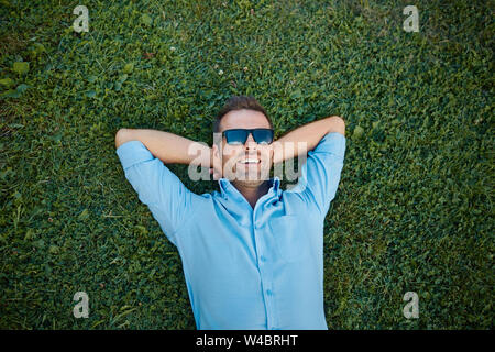 attractive man with sunglasses relaxing on the grass with his hands under the head Stock Photo
