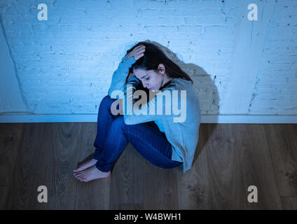 Portrait of young desperate latin woman feeling miserable, lonely, hopeless and sad sitting on the ground against a white wall with copy space and moo Stock Photo