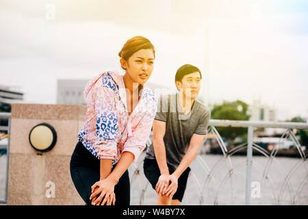 Asian man and woman looking away and doing lunges on bridge over river during workout on city street Stock Photo