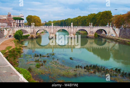 Image of Rione Ponte district. View of white Ponte Sant'Angelo bridge and its reflection, orange trees, green waters of Tiber river under dramatic clo Stock Photo