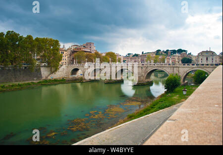 Image of Rione Ponte district. View of white Ponte Sant'Angelo bridge and its reflection, orange trees, green waters of Tiber river under dramatic clo Stock Photo