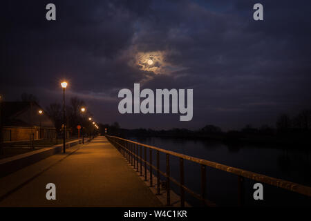 the full moon comes squeaking among the dramatic clouds on the Leie in Wervik, Belgium Stock Photo