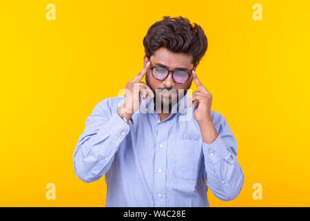 Young indian male professor with a beard in glasses and formal clothes is looking down thoughtfully posing on a yellow background. Concept of search Stock Photo