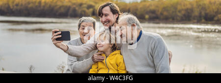 BANNER, LONG FORMAT Senior couple with with grandson and great-grandson take a selfie in the autumn park. Great-grandmother, great-grandfather and Stock Photo