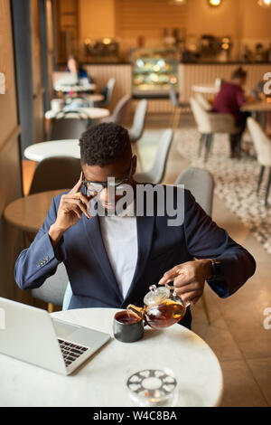 Afro-american working at the laptop and pouring himself tea. Stock Photo