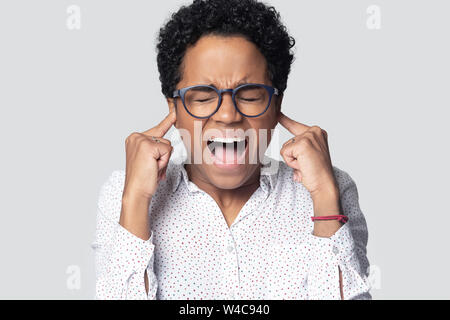 Stressed african American girl plug ears shout avoiding loud noise Stock Photo