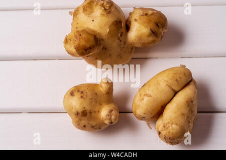 Flat lay Some ugly curved bent potatoes on white wooden background. Stock Photo