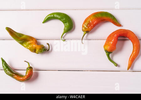 Flat lay Some ugly curved bent peppers on white wooden background. Stock Photo