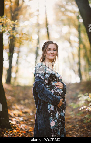 Portrait of smiling pregnant woman in colorful autumn forest. Stock Photo