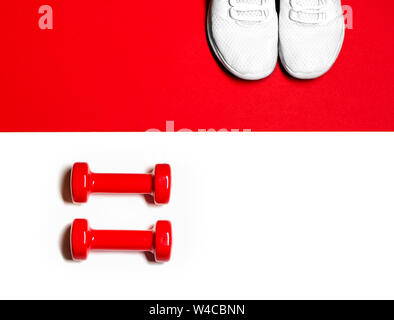 Flat lay composition with red dumbbells and white sneakers on red and white background. Fitness concept. Stock Photo