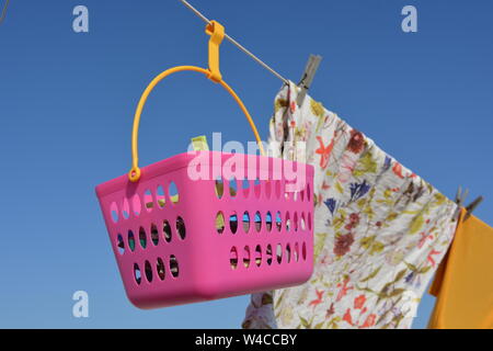 laundry hanging out to dry outdoors on a hot sunny, day. Close up, detail of pink peg basket, shirts and clothes pegs against blue sky background pegh Stock Photo