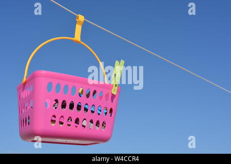 Laundry day. Pink peg basket hanging on the line against blue sky background with copy space. Stock Photo