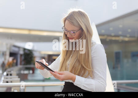Young blonde dedicated businesswoman in glasses using digital tablet in business center Stock Photo