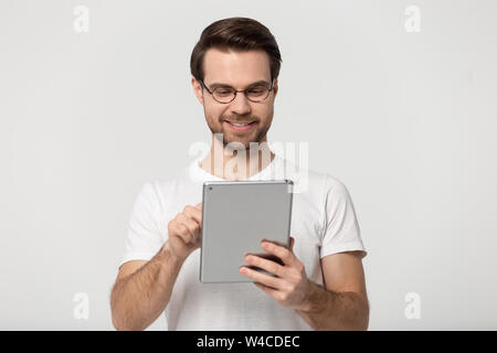 Millennial guy in glasses using tablet isolated on grey background Stock Photo