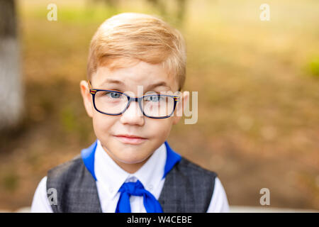 Educational theme: portrait of a schoolboy with big black glasses and blue tie. School backyard, beginning of classes. Stock Photo