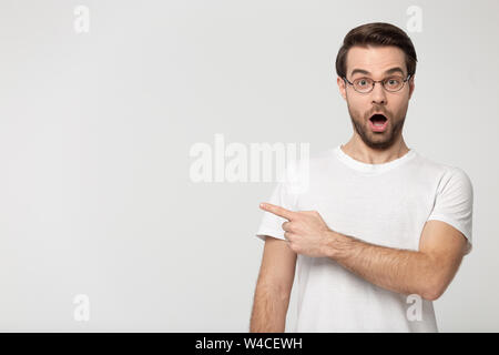 Surprised young man wearing glasses pointing finger aside at copyspace Stock Photo