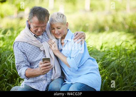 Portrait of loving senior couple looking at smartphone screen while enjoying date in park, copy space Stock Photo