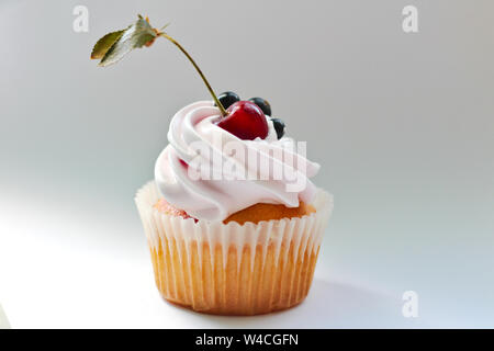 Isolated cupcake with cream, cherry with a leaf and black currant on a white background. Stock Photo