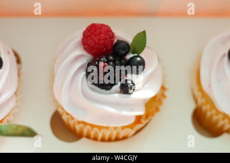 Isolated cupcake with cream, cherry with a leaf and black currant in a crafting box on a white background. Stock Photo
