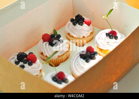 Isolated cupcakes with cream, cherry with a leaf, blackberry, raspberry black currant in a crafting box on a white background. Stock Photo