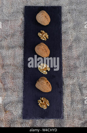 Walnuts, with and without shell, on black table surface, over sack texture Stock Photo