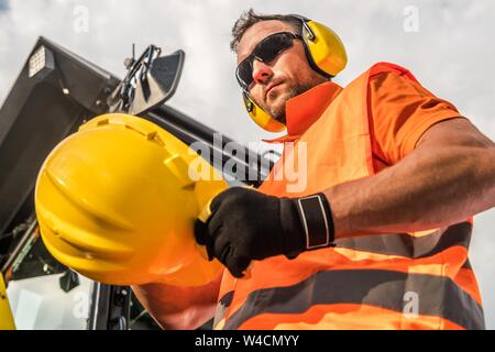 Caucasian Worker and the Machine. Yellow Hard Hat Head Protection. Stock Photo