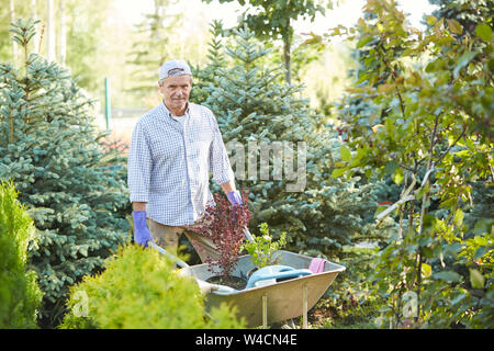 Portrait of mature man pulling cart while working in garden outdoors, copy space Stock Photo