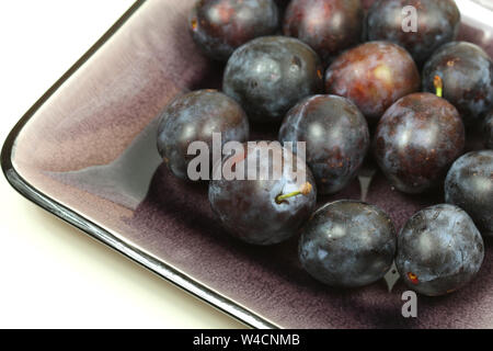 Plums on purple dish over white Stock Photo