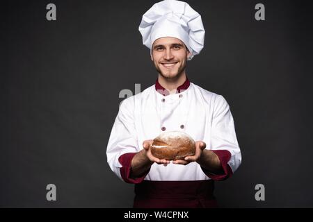 Male baker holding bread loaf and looking at camera isolated on black. Stock Photo