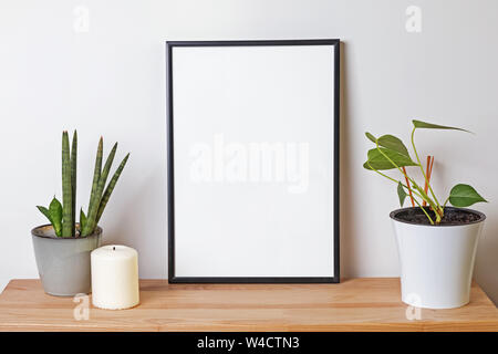 Blank frame mock-up in the wooden shelf with green plants over the white wall Stock Photo