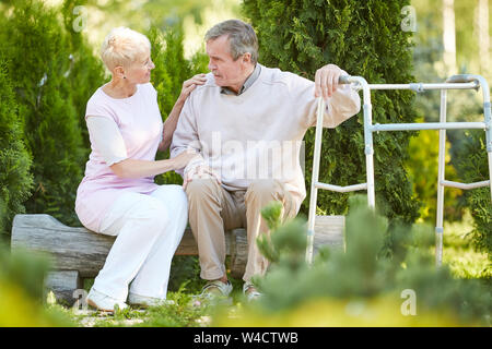 Full length portrait of senior man leaning on walker resting in park with caring nurse or wife, copy space Stock Photo