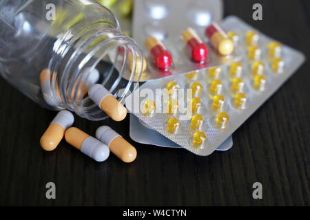 Pills in blister packs and capsules in transparent bottle on vintage dark wooden table. Concept of drugs, antibiotics, vitamins, pharmacy Stock Photo
