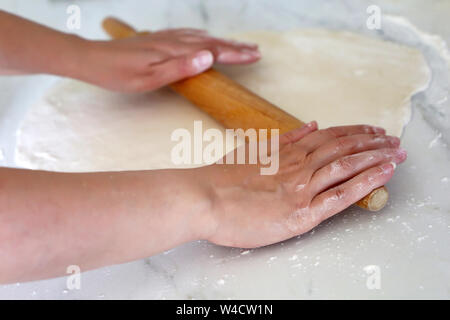 Rolling pin in female hands on a kitchen, woman rolls out the dough on a table. Concept of baker, cooking, housewife, baking of pie or pizza Stock Photo