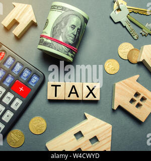 Wooden houses, a calculator, keys, coins and blocks with the word Tax. Property taxes. Calculation of interest on housing tax. Penalty, arrears. Regis Stock Photo