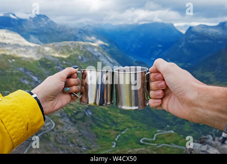 Woman and man hand holding together camping mugs with hot tea on the background of mountains Stock Photo