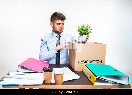 The young man is resigned and folds things in the workplace, folders, documents. Couldn't cope with responsibilities. Concept of office worker's troubles, business, advertising, resignation problems. Stock Photo